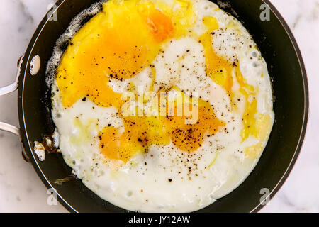 Fried eggs with pepper on top in a frying pan, top view. Stock Photo