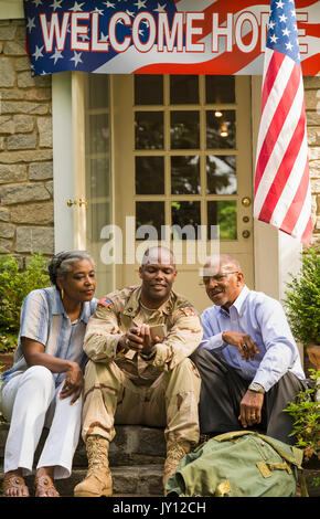 Soldier sitting on front stoop with parents and texting on cell phone Stock Photo