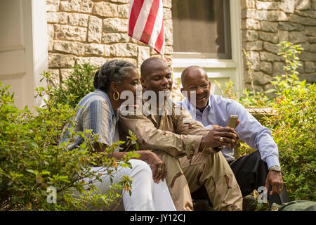 Soldier sitting on front stoop with parents and texting on cell phone Stock Photo