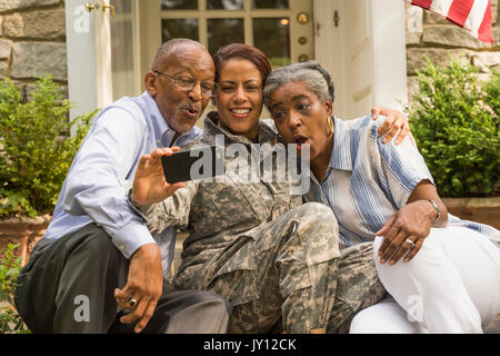 Soldier sitting on front stoop with parents and posing for cell phone selfie Stock Photo