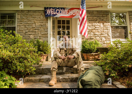 Frustrated African American soldier sitting on front stoop Stock Photo