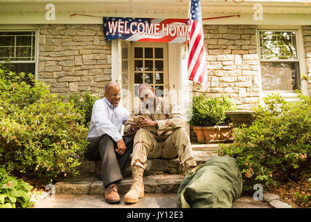 Soldier and father sitting on front stoop texting on cell phone Stock Photo