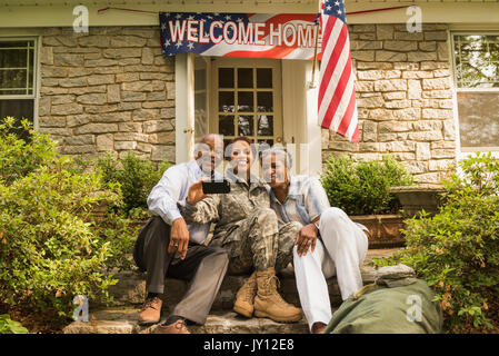 Soldier and parents sitting on front stoop posing for cell phone selfie Stock Photo