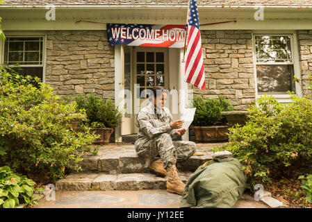 Smiling African American soldier sitting on front stoop reading letter Stock Photo