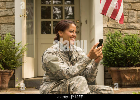 Smiling African American soldier sitting on front stoop texting on cell phone Stock Photo