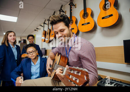 Male teacher is playing a guitar in his music lesson and his students are watching. Stock Photo