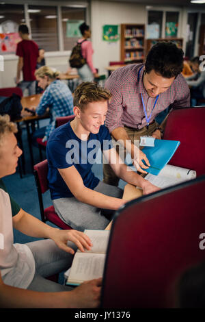Students are laughing as they work on computers together. There is a teacher leaning over their shoulder, helping them with their work. Stock Photo