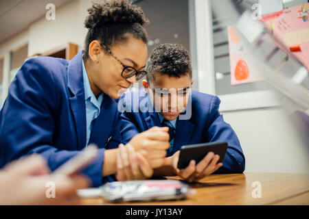 Two teen students are sneakily looking at a smart phone together during lesson time. Stock Photo