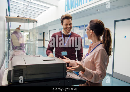 Two teachers are talking while standing at a printer in the school hall. Stock Photo