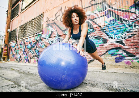 Hispanic woman balancing on fitness ball near graffiti wall Stock Photo