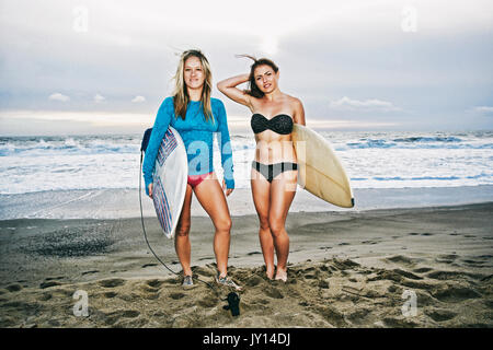 Caucasian women standing on beach holding surfboards Stock Photo