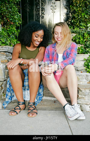 Friends siting on front stoop texting on cell phone Stock Photo