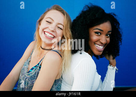 Friends sitting near blue wall laughing Stock Photo