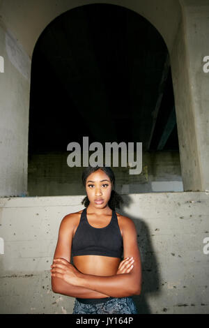 Mixed Race woman with arms crossed under overpass Stock Photo