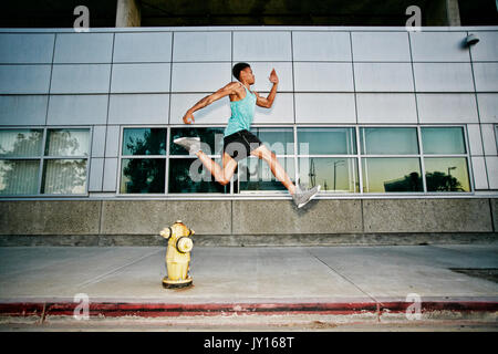 Black man running and jumping over fire hydrant Stock Photo