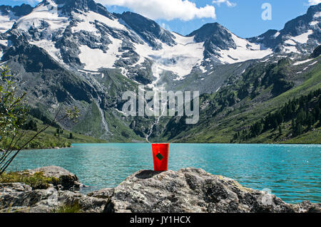 Tea bag in orange plastic Cup on the background of the beautiful landscape and blue lakes. Tourist Hiking romance. Breakfast in the nature. Stock Photo