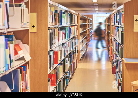 Student walking through a passage between the bookcases in the library Stock Photo