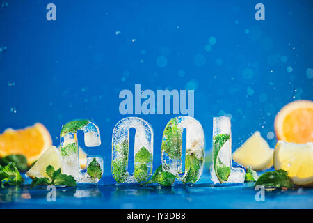 Ice cube lettering with frozen mint leaves, lemon slices and oranges on a blue background with water splashes. Text says Cool. Stock Photo