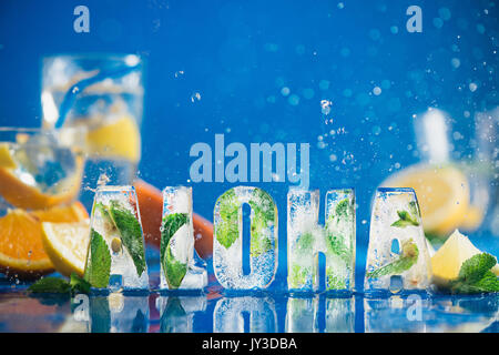 Ice cube lettering with frozen mint leaves, lemon slices and oranges on a blue background with water splashes. Text says Aloha. Stock Photo