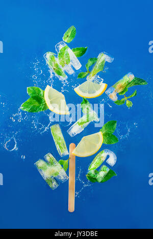Ice cube lettering with frozen mint leaves, lemon slices and oranges on a blue background with water splashes. Text says Melting. Stock Photo