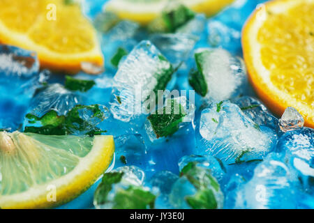 Close-up of sliced oranges and lemons on a blue background with ice cubes