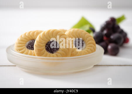 Blueberry Biscuits put on a ceramic plate and bunch of purple grapes placed close together on white wooden background, Selective focus. Stock Photo