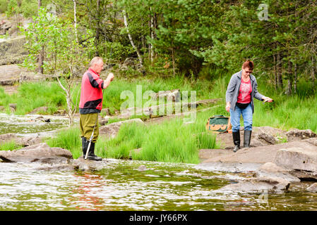 Byglandsfjord, Norway - August 1, 2017: Travel documentary of man preparing his fishing attire while woman carry freshly caught fish in hand. Forest i Stock Photo