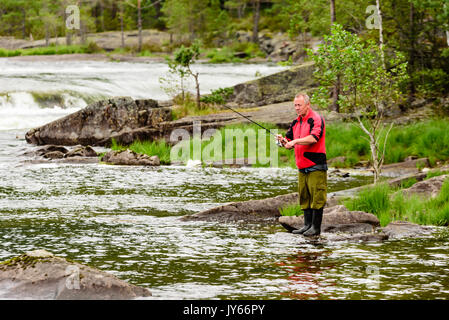 Byglandsfjord, Norway - August 1, 2017: Travel documentary of man standing on rock in water while fishing. Whitewater in background. Stock Photo