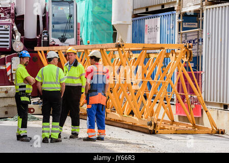 Kristiansand, Norway - August 1, 2017: Documentary of everyday life in the city. Group of construction workers having discussion. Crane parts on groun Stock Photo
