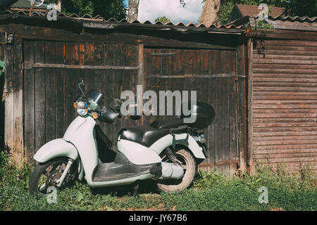 White Retro Vintage Sprint Motor Scooter Motorbike Motorcycle Bike Parked Against Wooden Shed Gates In Village. Sunny Summer Day. Stock Photo