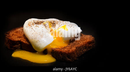 Poached egg on a slice of wholemeal bread. Photo on a black background Stock Photo