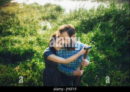 wife affectionately hugging husband on coast of lake in sunny morning Stock Photo