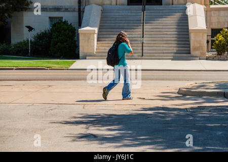 A young male college student with backpack on his cell phone while walking to class in Norman Oklahoma, home of the University of Oklahoma, Oklahoma,  Stock Photo