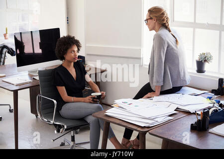 Two young businesswomen sit talking together in an office Stock Photo