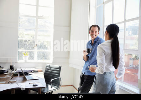 Two young business colleagues talk by window in an office Stock Photo