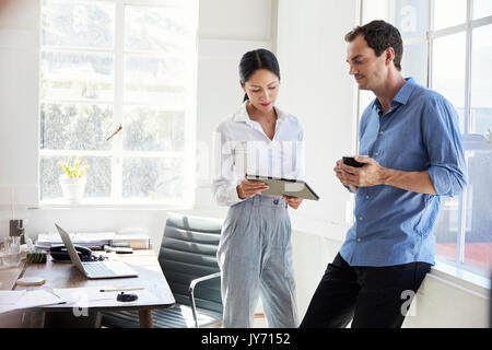 Two young business colleagues stand using tablet in office Stock Photo