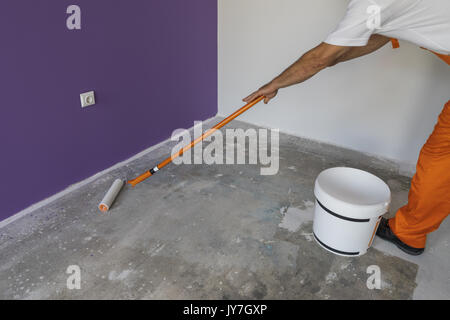 The hand of a man holding a roller and puts primer on concrete floor. Interior of a house under construction Stock Photo