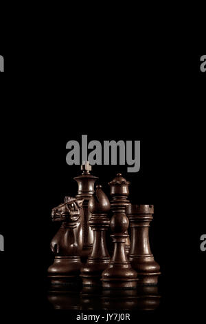 Creative business concept photo, black wooden chess figures standing together as a family ready for game against dark background. Stock Photo