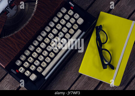 Overhead of vintage typewriter, diary and spectacles on wooden table Stock Photo