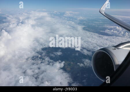 Airplane window view. View of clouds through airplane window. Above the clouds. Airplane window view of clouds and land from passenger seat. Vacation. Stock Photo