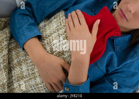 Mid section of woman with hot water bottle while sleeping on sofa at home Stock Photo