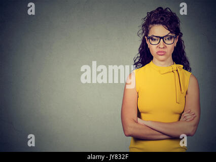 Portrait of angry woman in yellow dress standing with arms folded on gray background Stock Photo