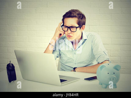 Serious young man in blue shirt looking at laptop while sitting at his working place Stock Photo