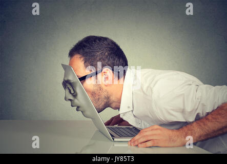 Young business man in glasses passing his head through a laptop screen Stock Photo