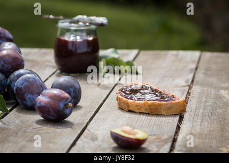 Sandwich with plum jam on old wooden table in garden. Stock Photo
