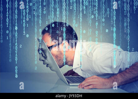 Side profile of a young business man with his face passing through the screen of a laptop on binary code background Stock Photo
