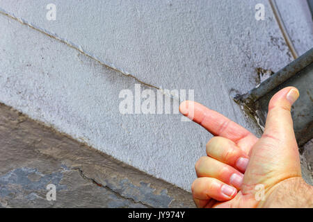 Human hand pointing at small cracks in plaster on the outside wall of a house. Building damage caused by weather. Stock Photo
