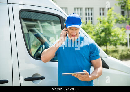 Male Worker In Front Truck Using Mobile Phone While Looking At Digital Tablet Stock Photo