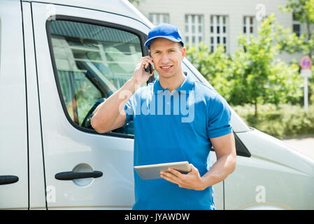 Male Worker In Front Truck Using Mobile Phone While Looking At Digital Tablet Stock Photo