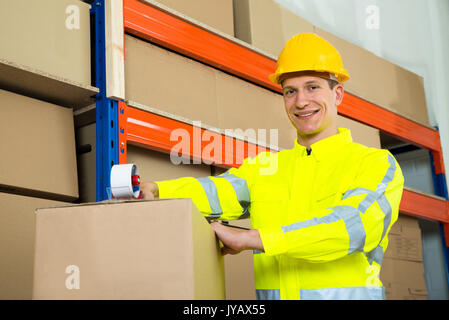 Male Worker Sealing Cardboard Box With Adhesive Tape In Warehouse Stock Photo